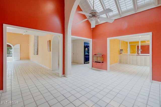 spare room featuring baseboards, arched walkways, tile patterned floors, high vaulted ceiling, and a ceiling fan