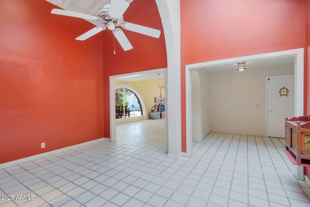 unfurnished room with ceiling fan, baseboards, a towering ceiling, and tile patterned floors