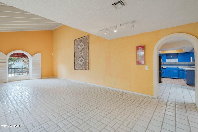 spare room featuring visible vents, a textured ceiling, arched walkways, light tile patterned floors, and baseboards