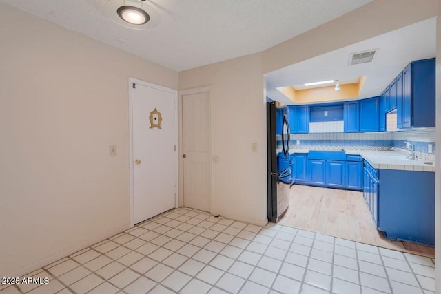 kitchen featuring visible vents, a tray ceiling, freestanding refrigerator, blue cabinets, and a sink