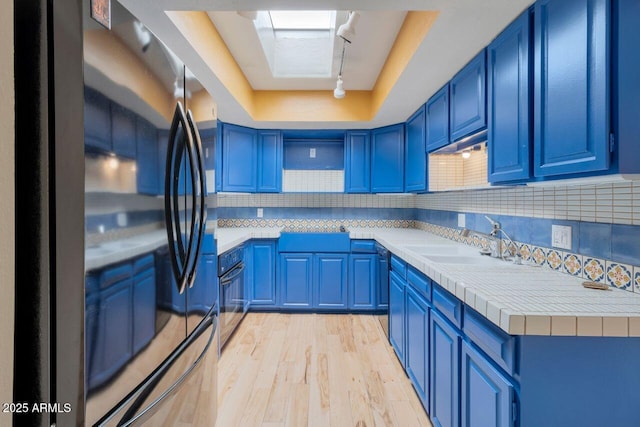 kitchen featuring blue cabinetry, a tray ceiling, tasteful backsplash, and freestanding refrigerator