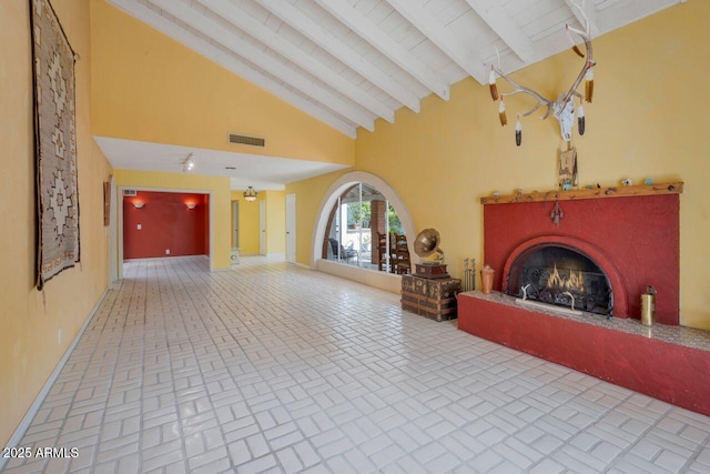 unfurnished living room with visible vents, a lit fireplace, beam ceiling, brick floor, and high vaulted ceiling