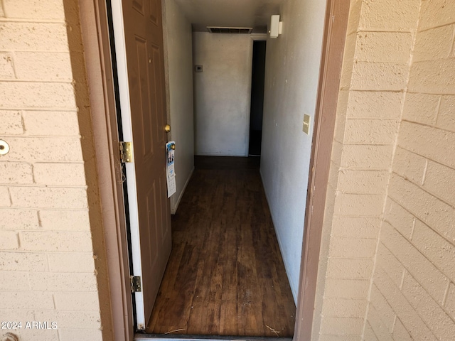 corridor with dark wood-type flooring and brick wall