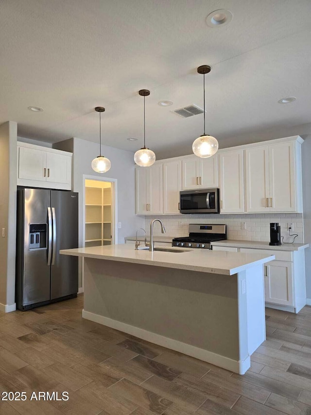 kitchen featuring wood finish floors, a sink, white cabinetry, appliances with stainless steel finishes, and decorative backsplash