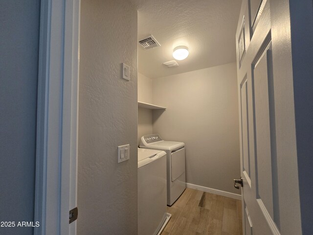 laundry area with laundry area, visible vents, a textured wall, washing machine and clothes dryer, and light wood-type flooring