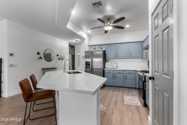 kitchen featuring ceiling fan, sink, light hardwood / wood-style floors, a kitchen bar, and appliances with stainless steel finishes