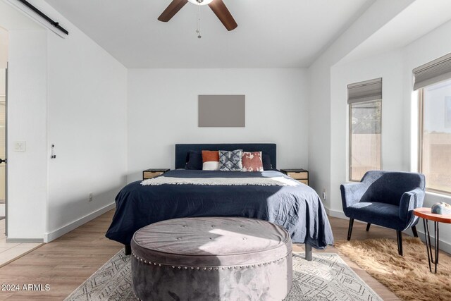 bedroom featuring a barn door, ceiling fan, and light hardwood / wood-style flooring