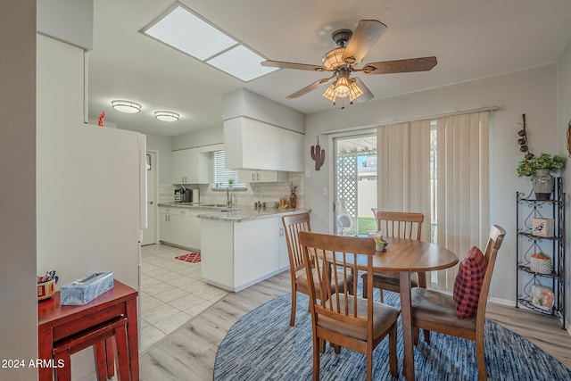 tiled dining room featuring ceiling fan, sink, and a skylight