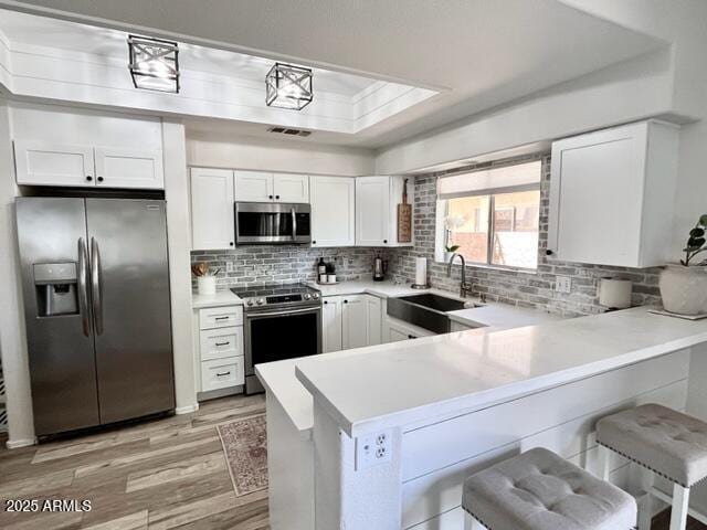 10229 N 12th Ct Unit 1, Phoenix, AZ 85020 - kitchen with appliances with stainless steel finishes, a sink, light wood finished floors, a peninsula, and white cabinetry