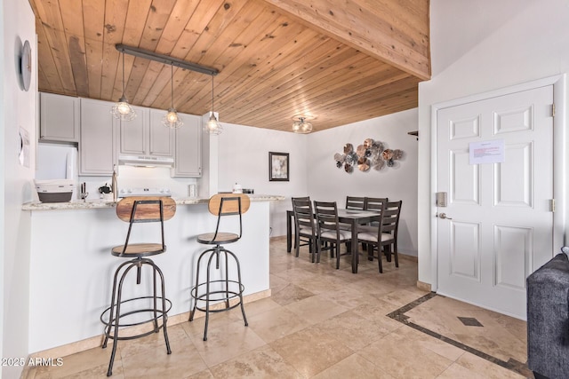 kitchen featuring a peninsula, white fridge, under cabinet range hood, wooden ceiling, and a breakfast bar area