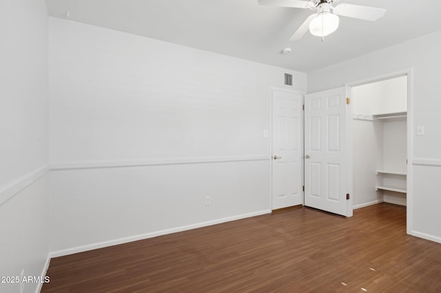 unfurnished bedroom with a closet, dark hardwood / wood-style floors, ceiling fan, and a spacious closet