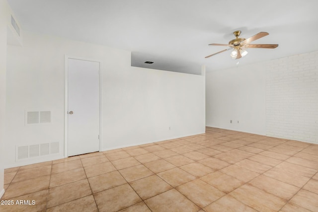 spare room with brick wall, light tile patterned floors, and ceiling fan