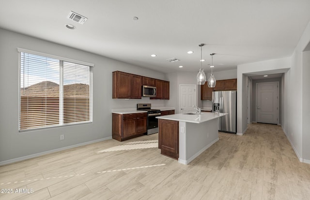 kitchen featuring dark brown cabinetry, sink, decorative light fixtures, an island with sink, and stainless steel appliances