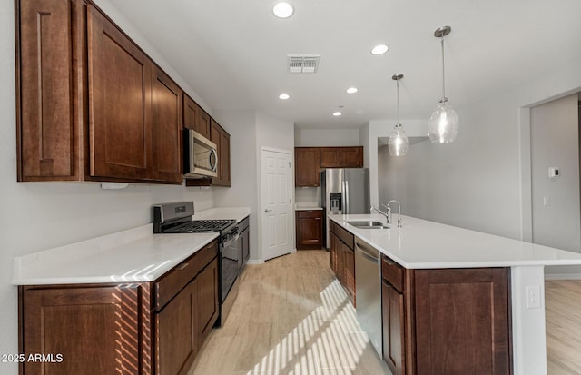 kitchen with appliances with stainless steel finishes, sink, hanging light fixtures, dark brown cabinetry, and a center island with sink