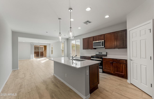 kitchen featuring sink, decorative light fixtures, dark brown cabinets, stainless steel appliances, and a kitchen island with sink