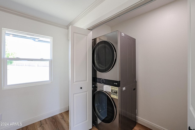 clothes washing area with stacked washer and clothes dryer, ornamental molding, wood finished floors, baseboards, and laundry area