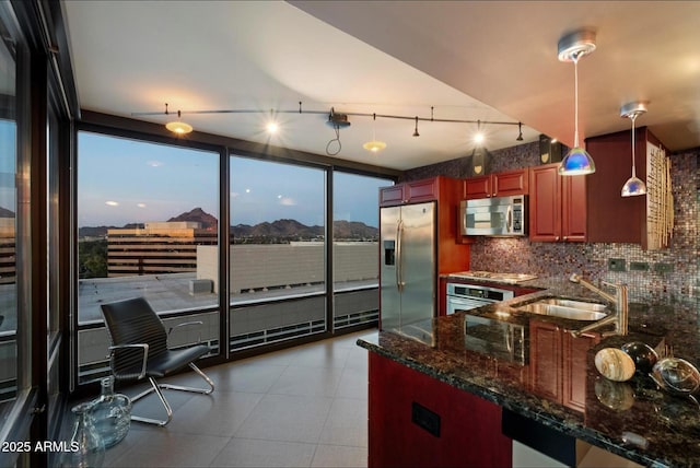 kitchen with decorative light fixtures, dark stone countertops, decorative backsplash, a sink, and appliances with stainless steel finishes