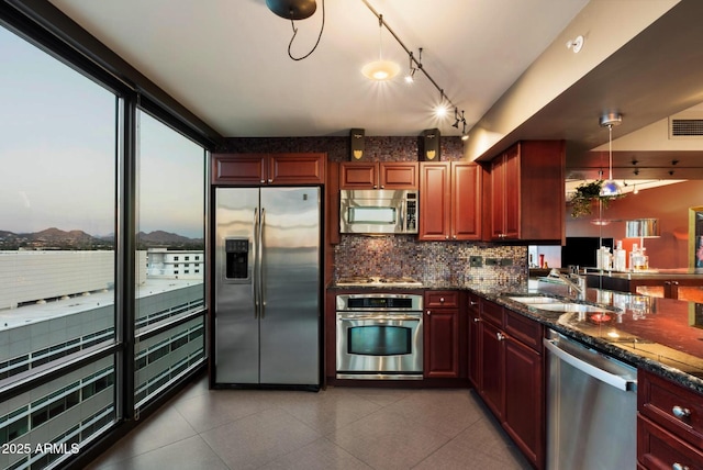kitchen featuring stainless steel appliances, tasteful backsplash, reddish brown cabinets, dark stone countertops, and a sink