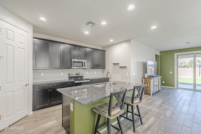 9934 E Orange Grove St, Florence, AZ 85132 - kitchen featuring stainless steel appliances, light wood-type flooring, stone countertops, backsplash, and a center island with sink