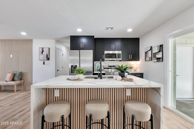 kitchen with visible vents, light stone countertops, stainless steel appliances, dark cabinetry, and a sink