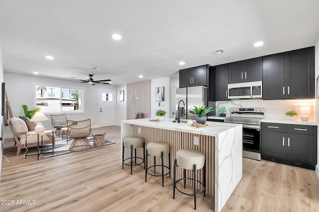 kitchen with light wood finished floors, a kitchen bar, stainless steel appliances, and a kitchen island with sink