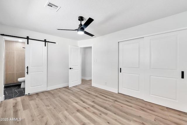 unfurnished bedroom with ensuite bathroom, a barn door, wood finished floors, visible vents, and a closet