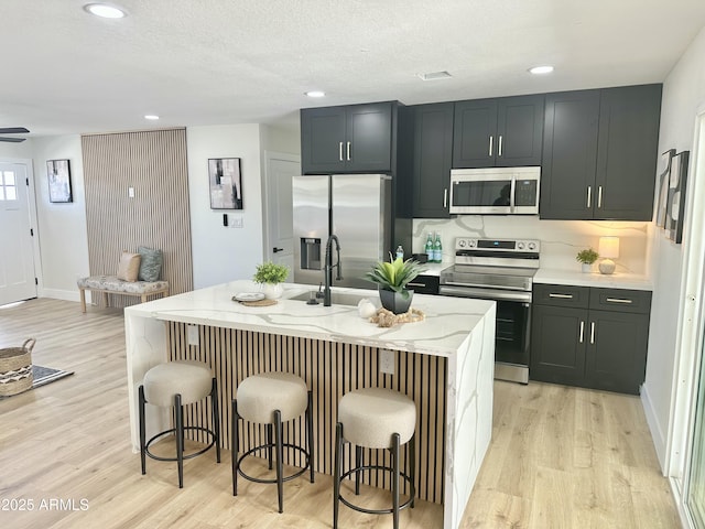 kitchen with appliances with stainless steel finishes, light wood-style flooring, a breakfast bar area, and light stone countertops