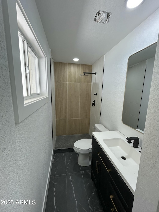 bathroom featuring baseboards, toilet, marble finish floor, a tile shower, and vanity