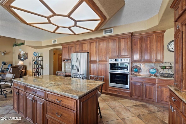 kitchen featuring a center island, stainless steel appliances, light stone counters, backsplash, and a breakfast bar