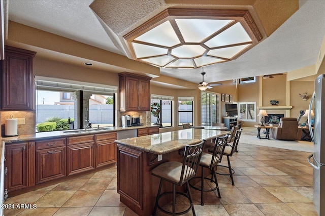 kitchen featuring a center island, ceiling fan, stainless steel fridge, light stone counters, and a kitchen bar