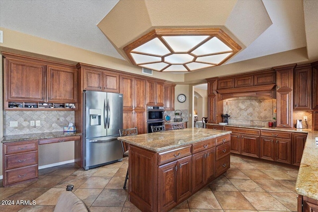 kitchen with tasteful backsplash, light stone counters, a kitchen island, and stainless steel appliances