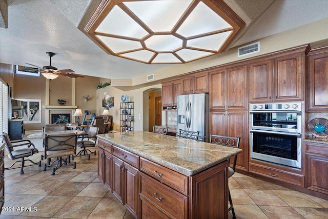 kitchen featuring light stone countertops, stainless steel appliances, ceiling fan, a kitchen island, and light tile patterned flooring