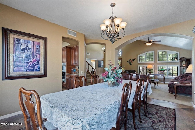 dining space with a textured ceiling, ceiling fan with notable chandelier, dark tile patterned flooring, and lofted ceiling