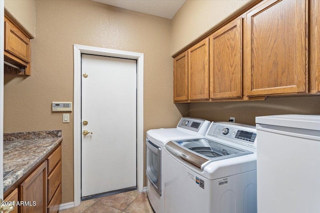 clothes washing area with separate washer and dryer, light tile patterned floors, and cabinets