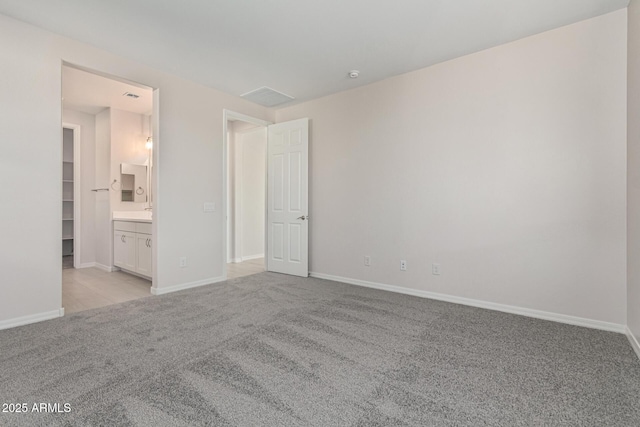 unfurnished bedroom featuring light carpet, ensuite bath, and a spacious closet