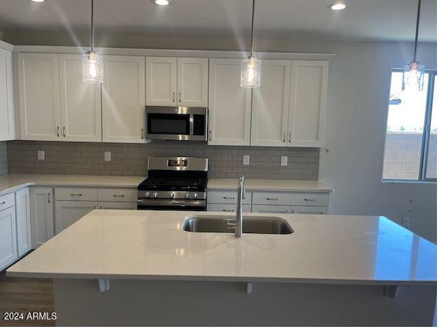 kitchen featuring hanging light fixtures, sink, stainless steel appliances, and a center island with sink