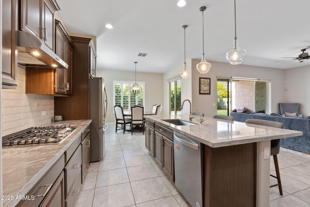 kitchen with a breakfast bar, a sink, stainless steel appliances, decorative backsplash, and under cabinet range hood