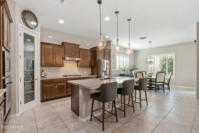 kitchen featuring light tile patterned flooring, a breakfast bar area, stainless steel appliances, under cabinet range hood, and visible vents