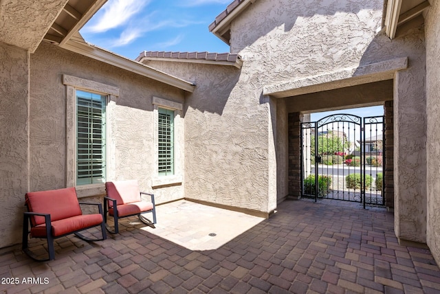 doorway to property with a gate, a patio area, and stucco siding