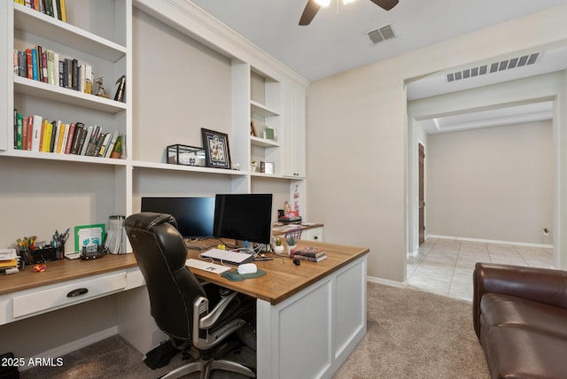 home office featuring a ceiling fan, light colored carpet, visible vents, and built in desk