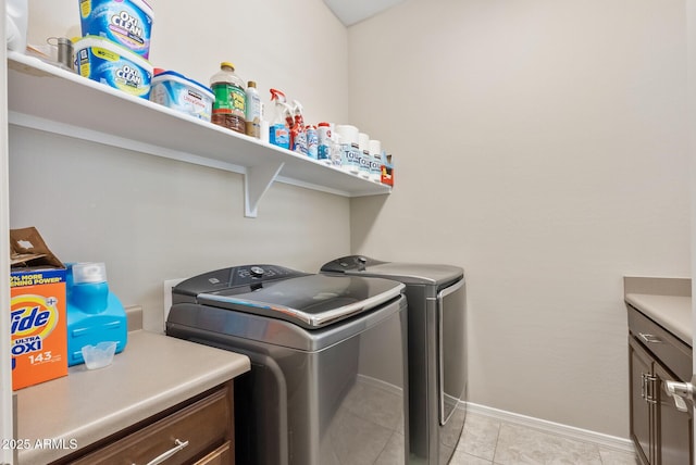 clothes washing area featuring light tile patterned floors, baseboards, cabinet space, and washer and clothes dryer