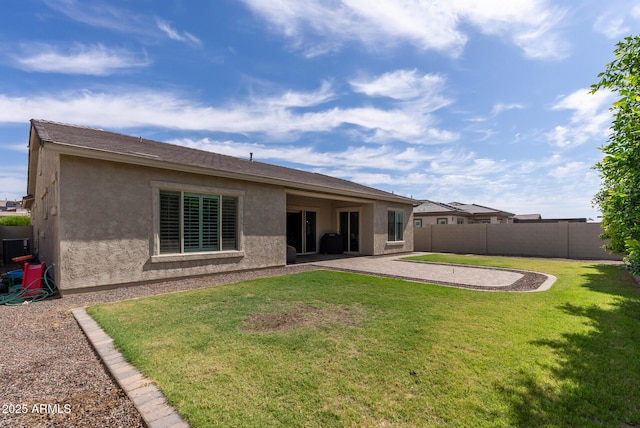rear view of property with fence, stucco siding, a lawn, and a patio area