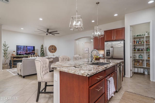 kitchen with sink, an island with sink, pendant lighting, ceiling fan with notable chandelier, and appliances with stainless steel finishes