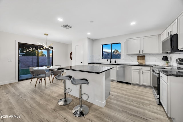 kitchen featuring stainless steel appliances, white cabinetry, a center island, and pendant lighting