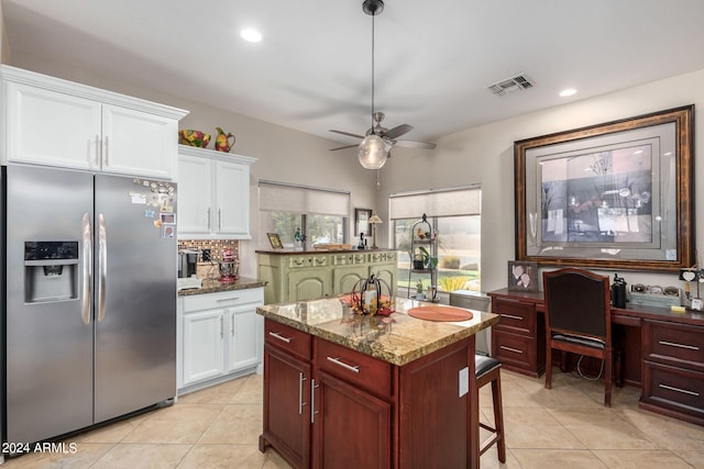 kitchen with ceiling fan, stainless steel fridge, white cabinetry, and a center island