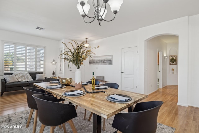 dining area featuring visible vents, baseboards, light wood-style flooring, arched walkways, and a notable chandelier