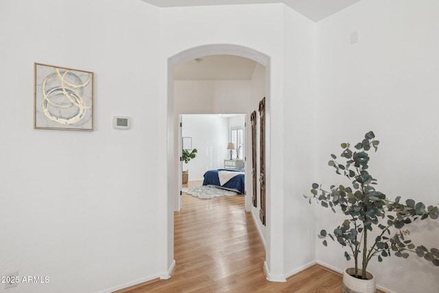 hall featuring baseboards, arched walkways, and light wood finished floors