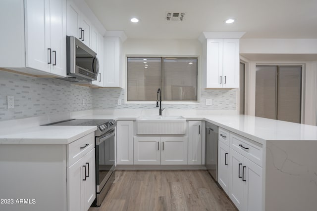 kitchen with light wood-type flooring, light stone counters, sink, white cabinets, and appliances with stainless steel finishes