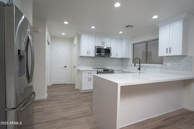 kitchen with light hardwood / wood-style flooring, stainless steel appliances, white cabinetry, and kitchen peninsula