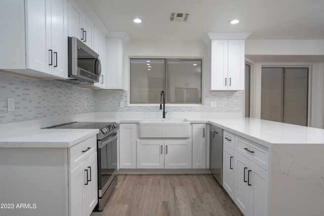 kitchen featuring white cabinets, sink, kitchen peninsula, stainless steel appliances, and light wood-type flooring